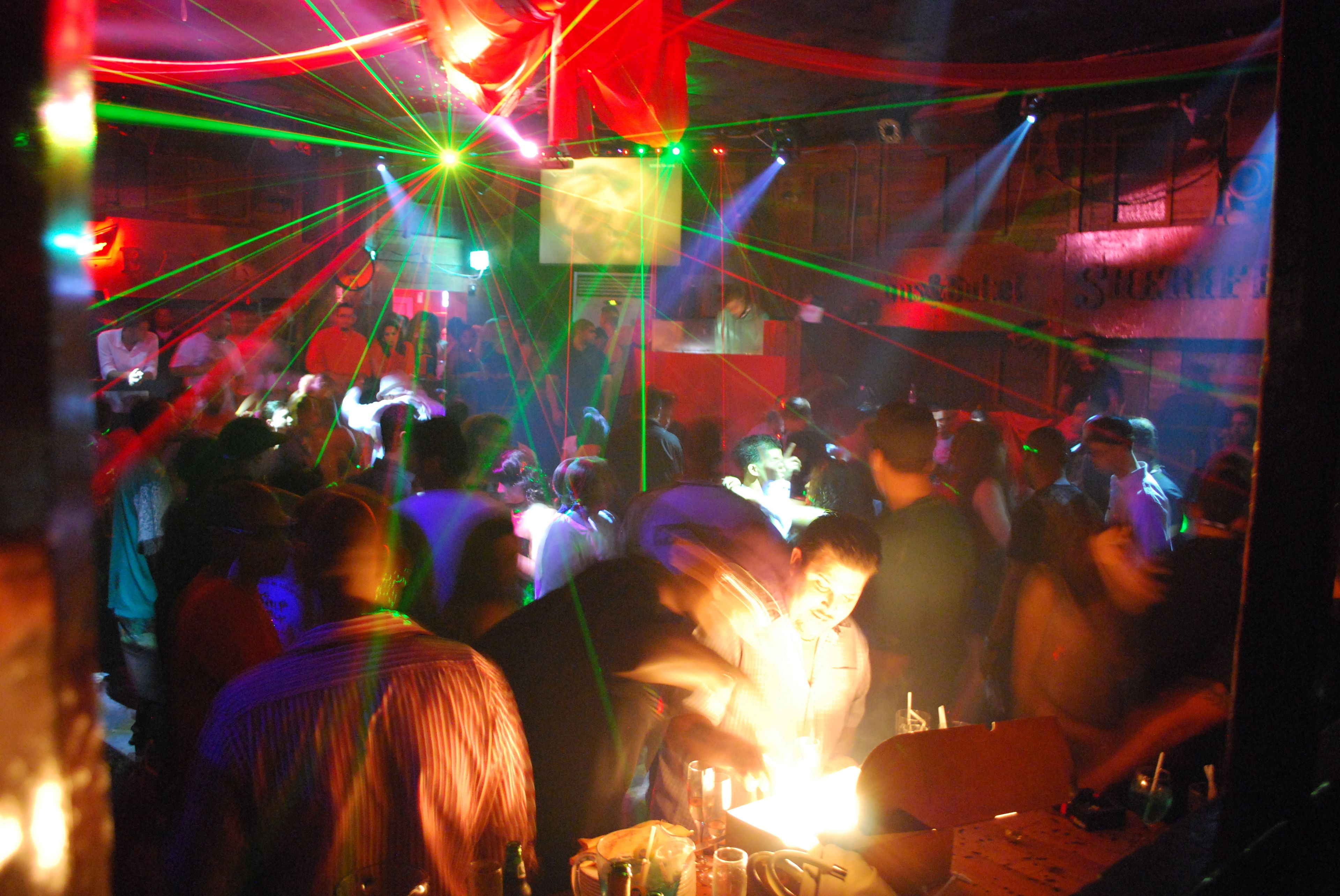 A crowded indoor venue with people, tables, and a stage.