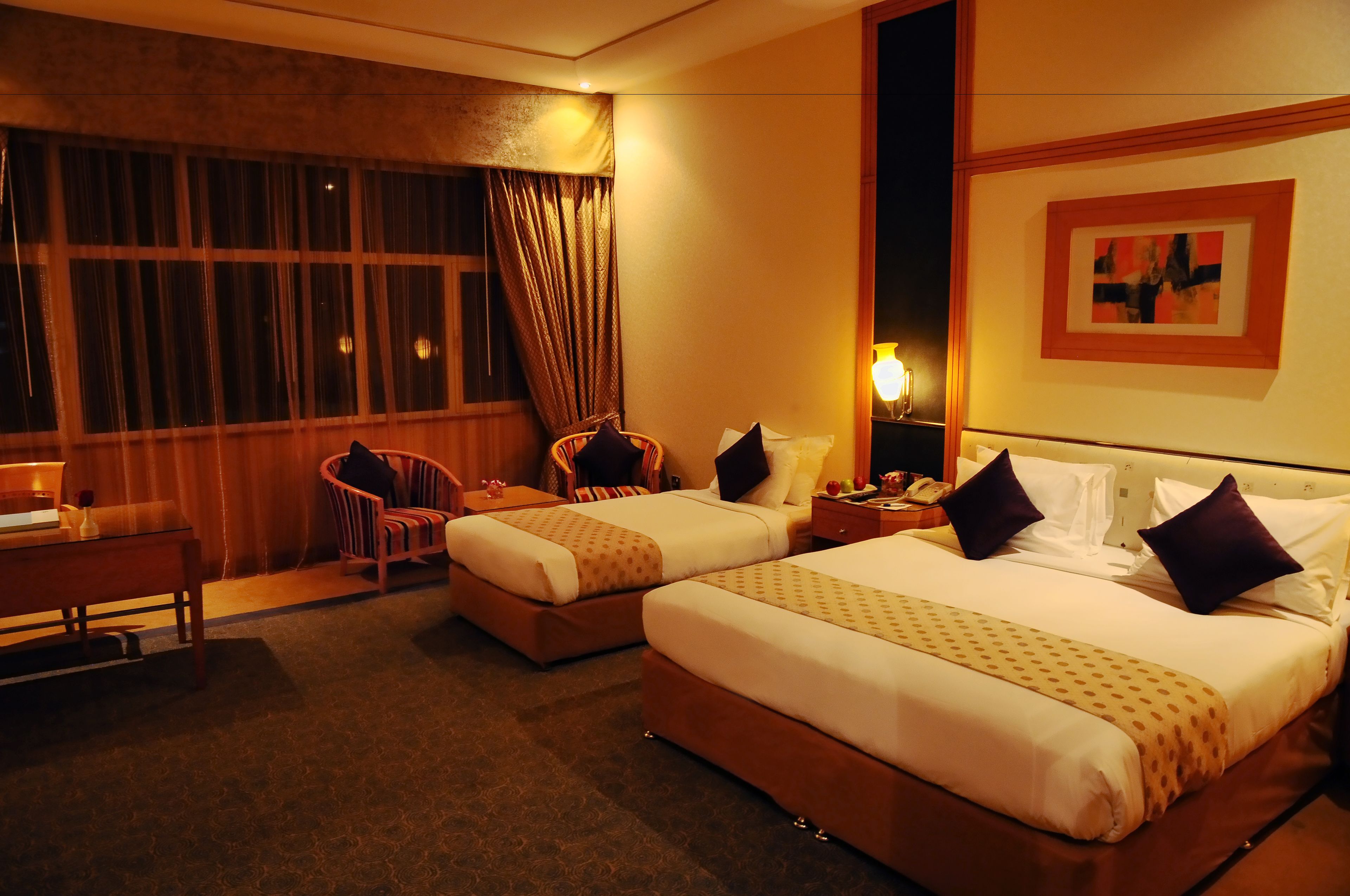 A hotel room with two beds, a desk, a chair, and a window with curtains.