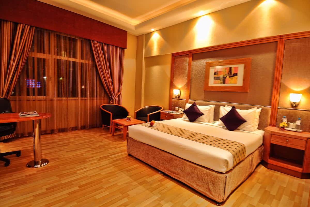 A hotel room with a large bed, a desk with a chair, a small table, and a nightstand.