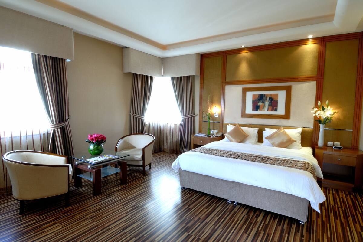 A hotel room with a large bed, two chairs, a small table with a vase of flowers, and a nightstand with a lamp.