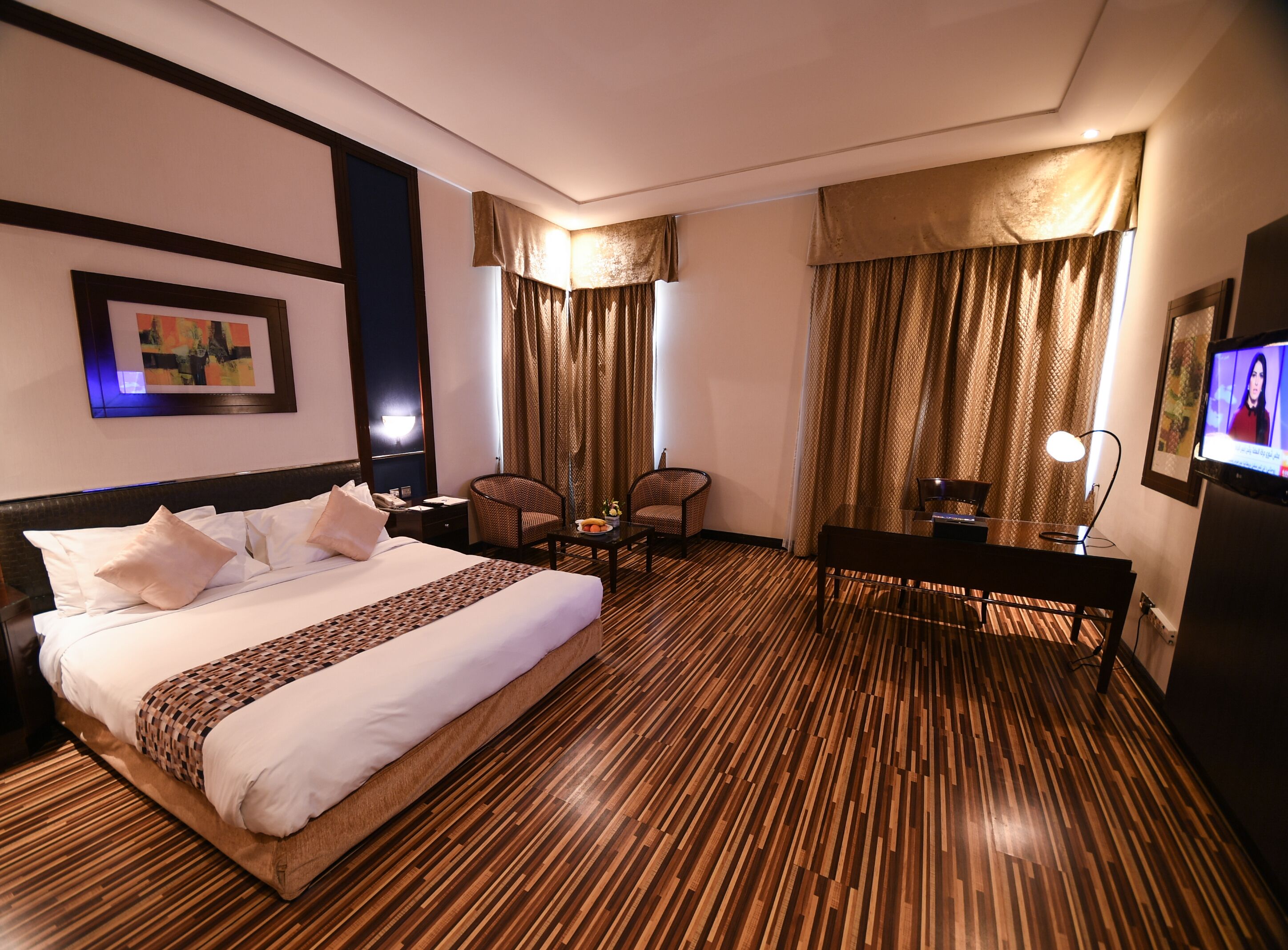 A hotel room with a large bed, two armchairs, a desk, a television, and a wooden floor.