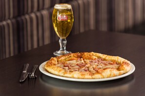 A pizza on a white plate with a glass of beer in the background. - Holiday Inn Express London - Dartford by IHG (Dartford)