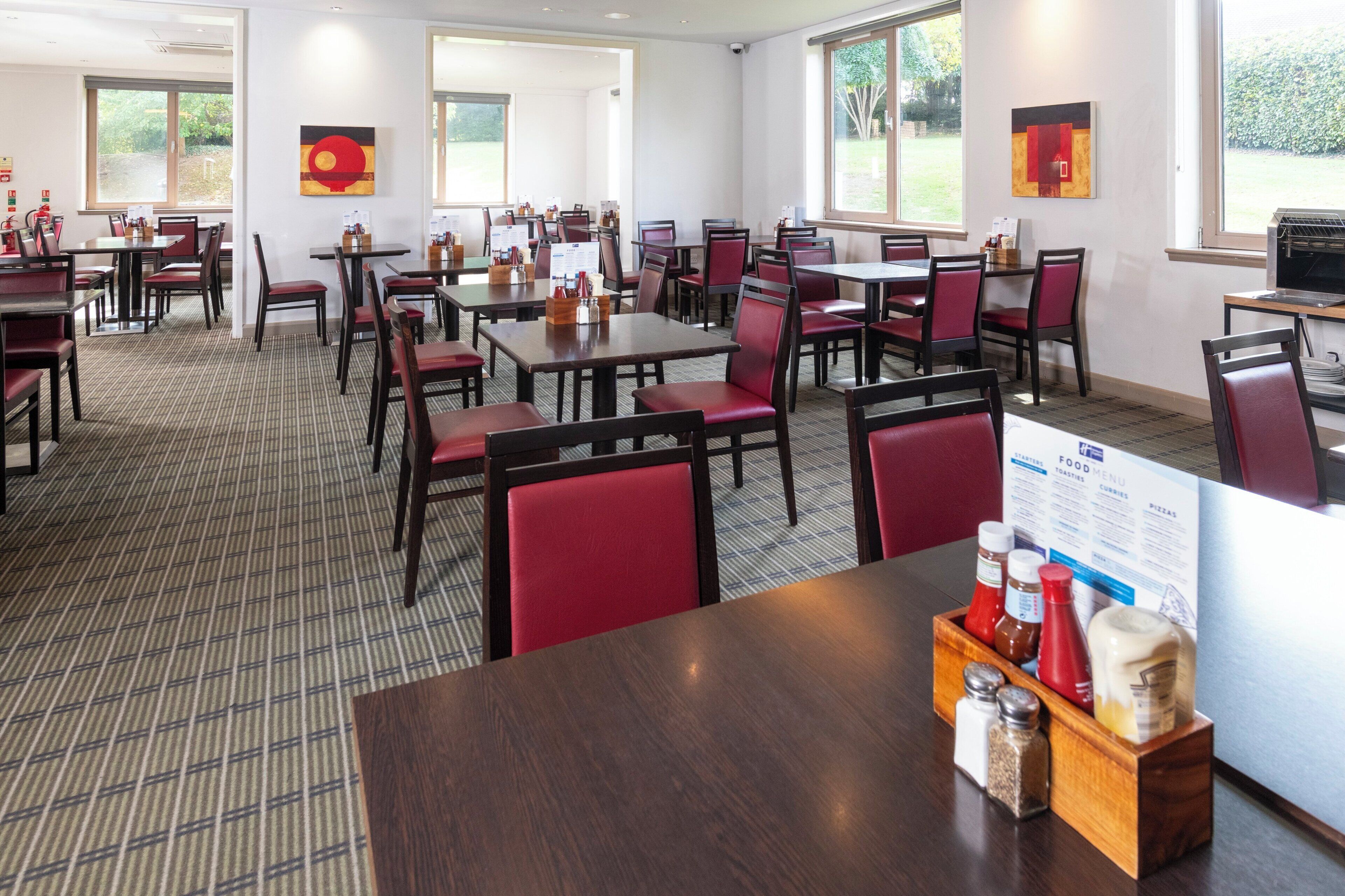 A hotel dining area with multiple tables and chairs, a food menu sign, and a window view.