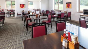 A hotel dining area with multiple tables and chairs, a food menu sign, and a window view.
