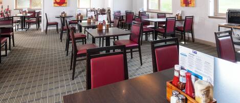 A hotel dining area with multiple tables and chairs, a food menu sign, and a window view.
