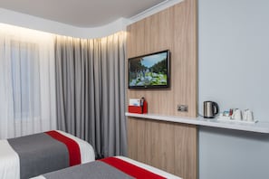 A hotel room with two beds, a television mounted on the wall, a wooden panel, a white shelf with a kettle and cups, and a red and grey bedspread. - Holiday Inn Express London - Dartford by IHG (Dartford)