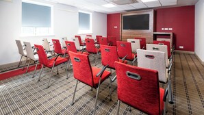 A conference room with rows of red and beige chairs, a large screen, and a carpeted floor. - Holiday Inn Express London - Dartford by IHG (Dartford)