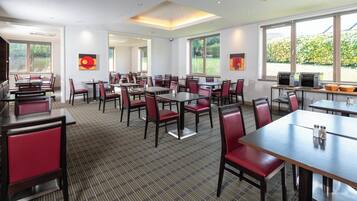 Une salle à manger d’hôtel avec de nombreuses tables et chaises, de grandes fenêtres et une vue sur la verdure environnante.