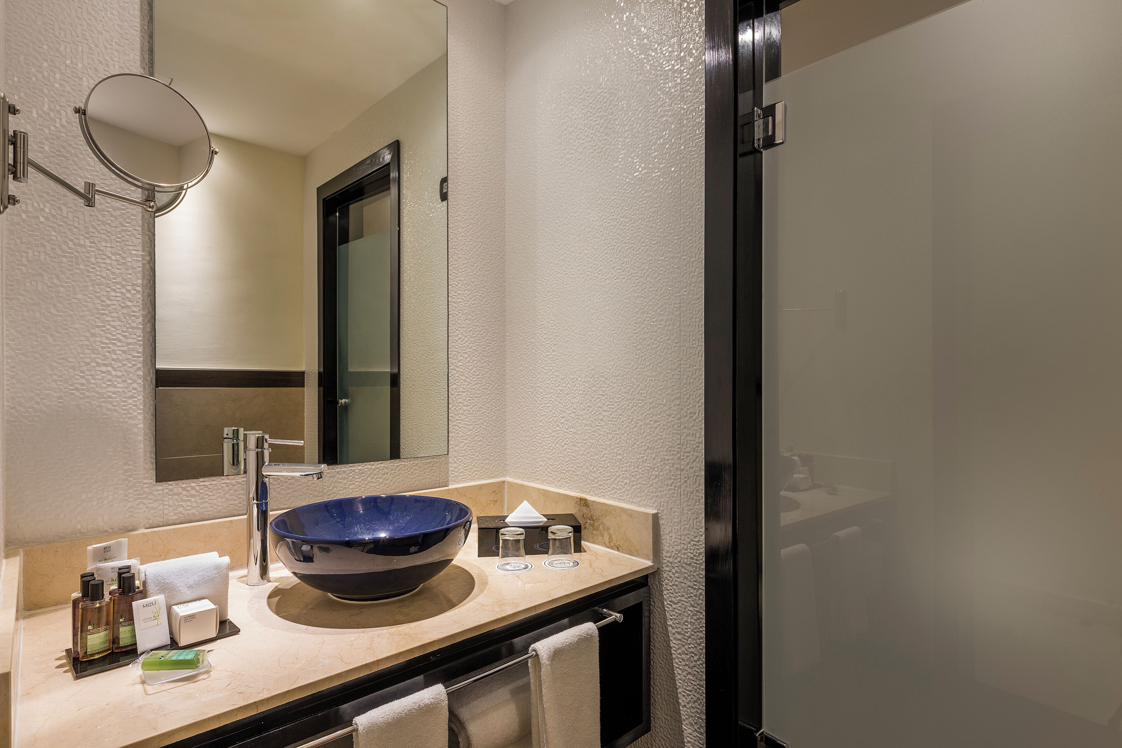 A bathroom with a large blue bowl sink, a mirror, a towel rack, and toiletries on the counter.