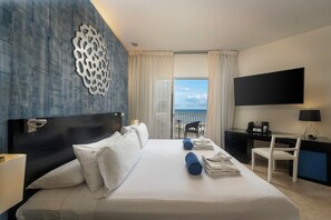 A hotel room with a large bed, a flat-screen TV, a desk, and a view of the sea. - Ocean Maya Royale - Adults Only -  All Inclusive  (Playa del Carmen)
