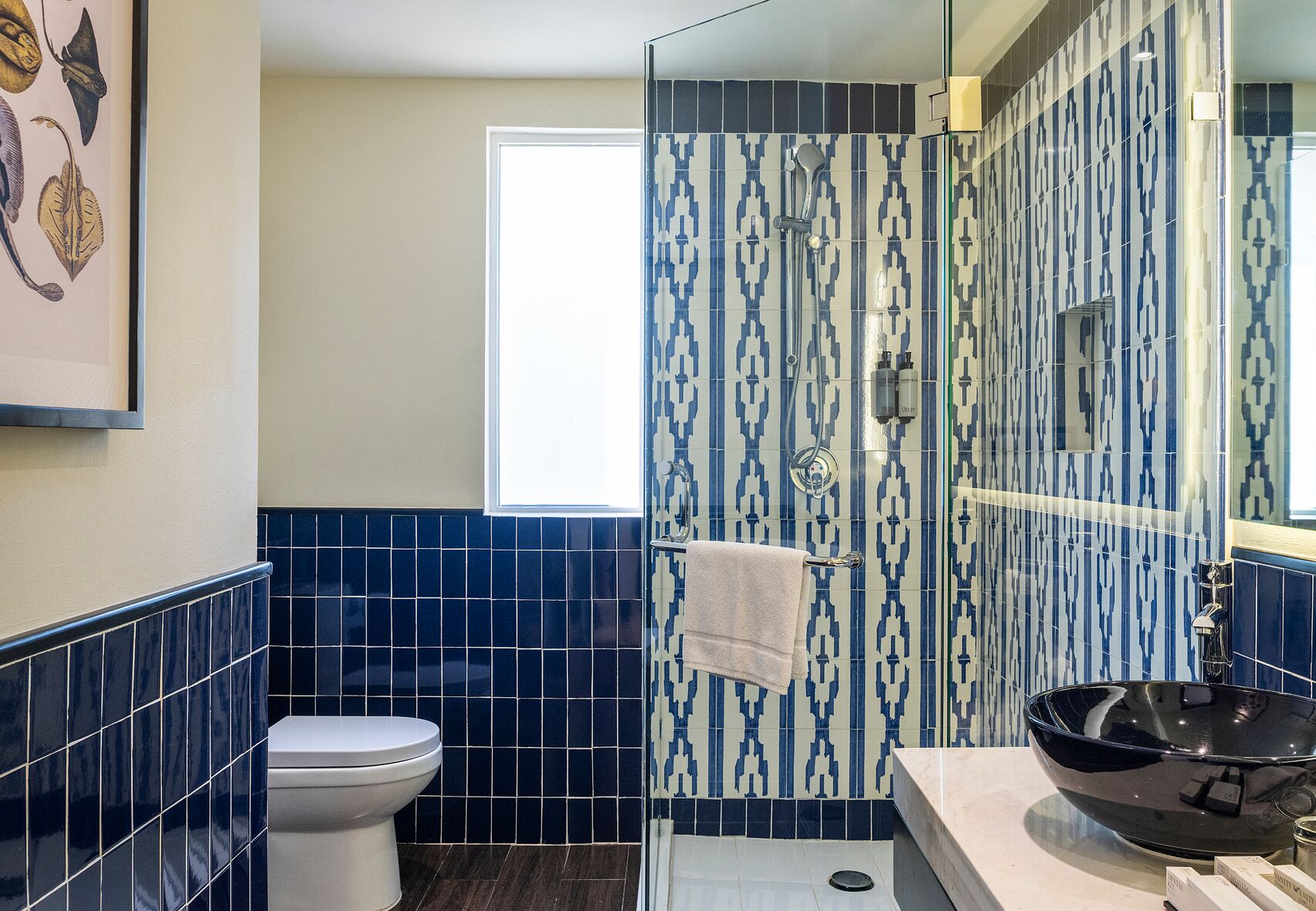 A bathroom with a toilet, a sink with a black basin, and a shower area with patterned tiles.