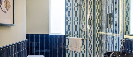 A bathroom with a toilet, a sink with a black basin, and a shower area with patterned tiles.