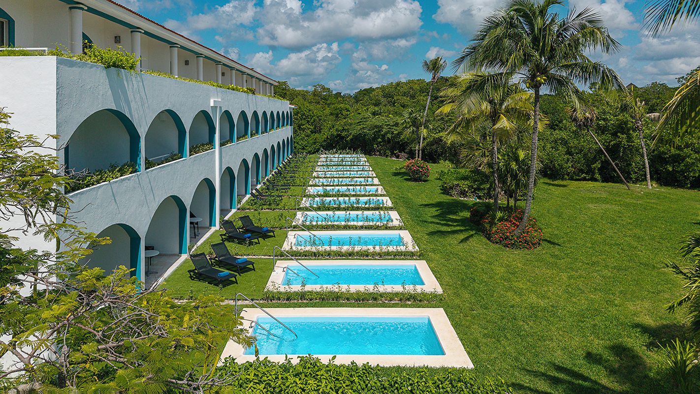Un resort con varias piscinas alineadas, rodeado de exuberante vegetación y palmeras.