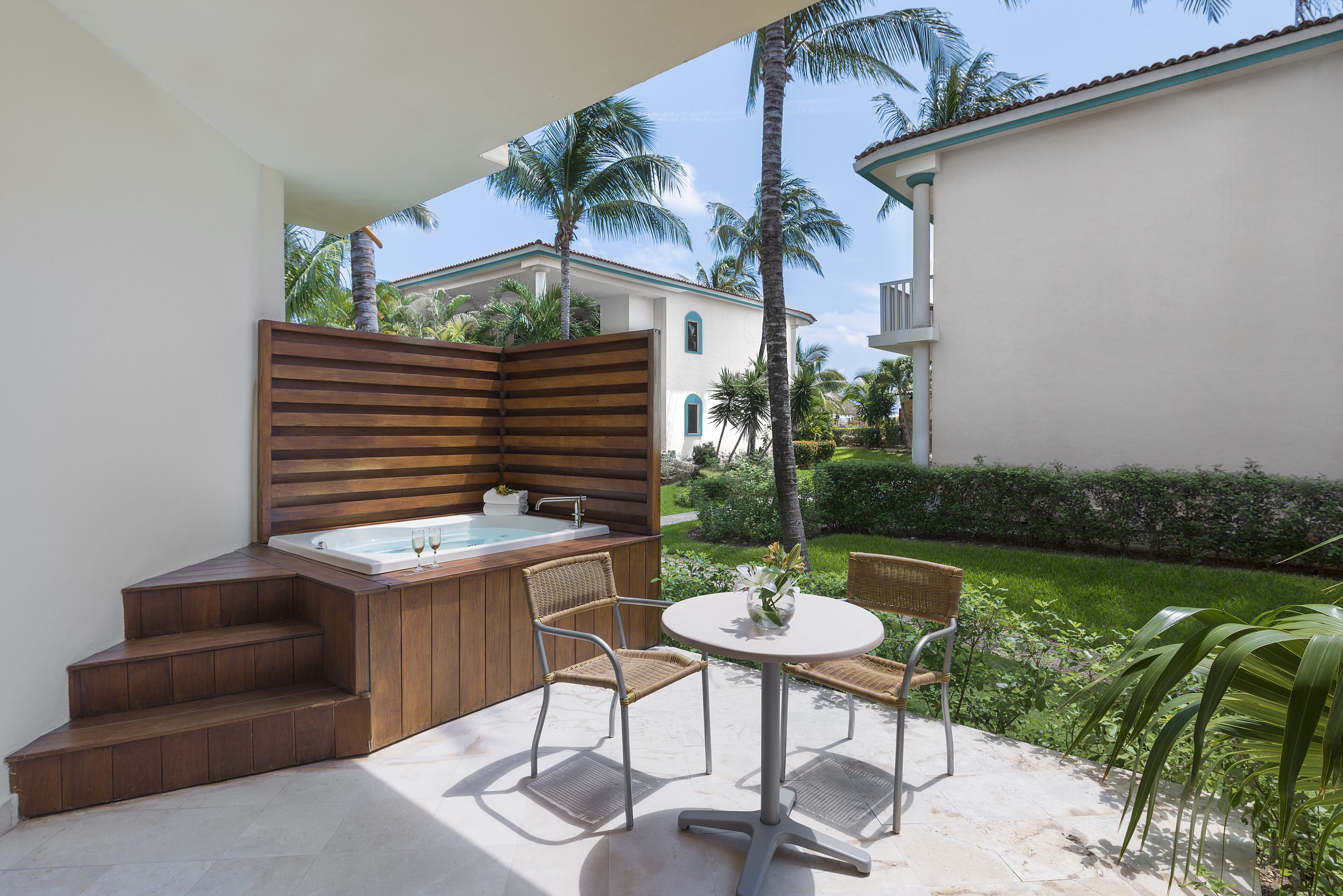 A patio with a hot tub, wooden steps, and wicker chairs.