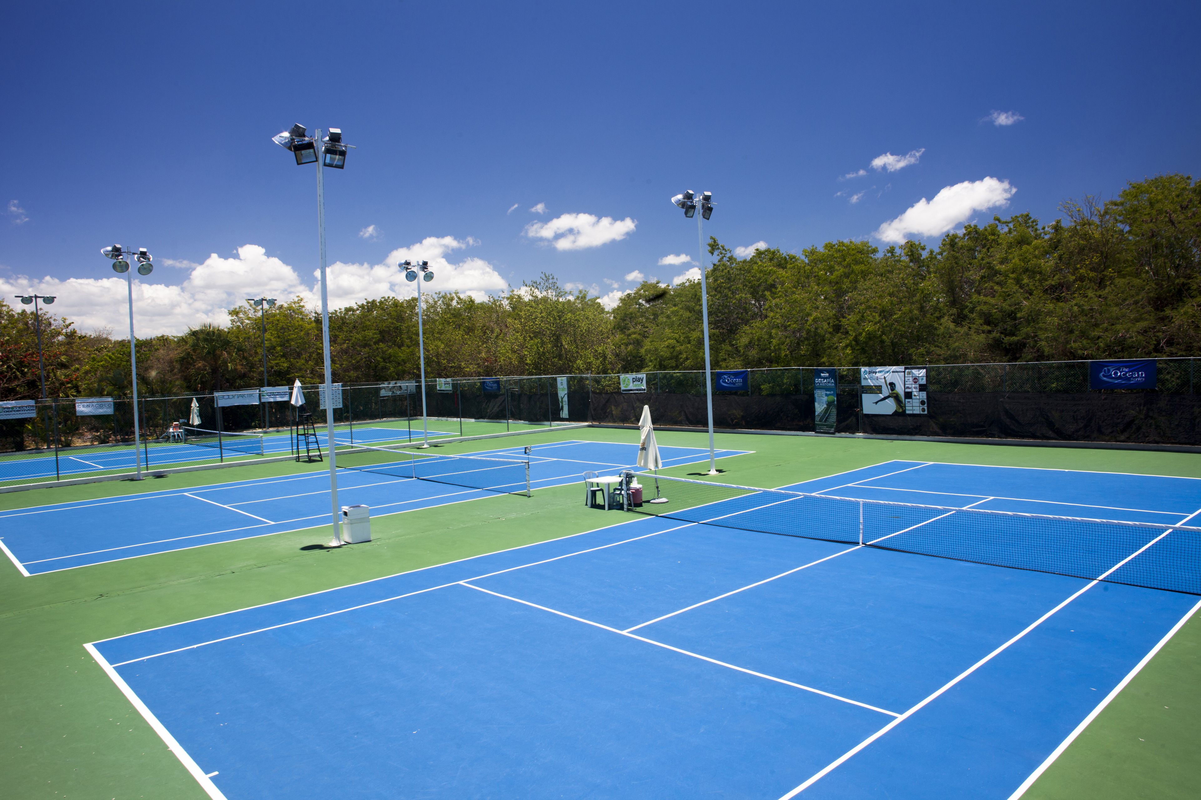 Un court de tennis comprenant plusieurs terrains, un système d’éclairage et une clôture.