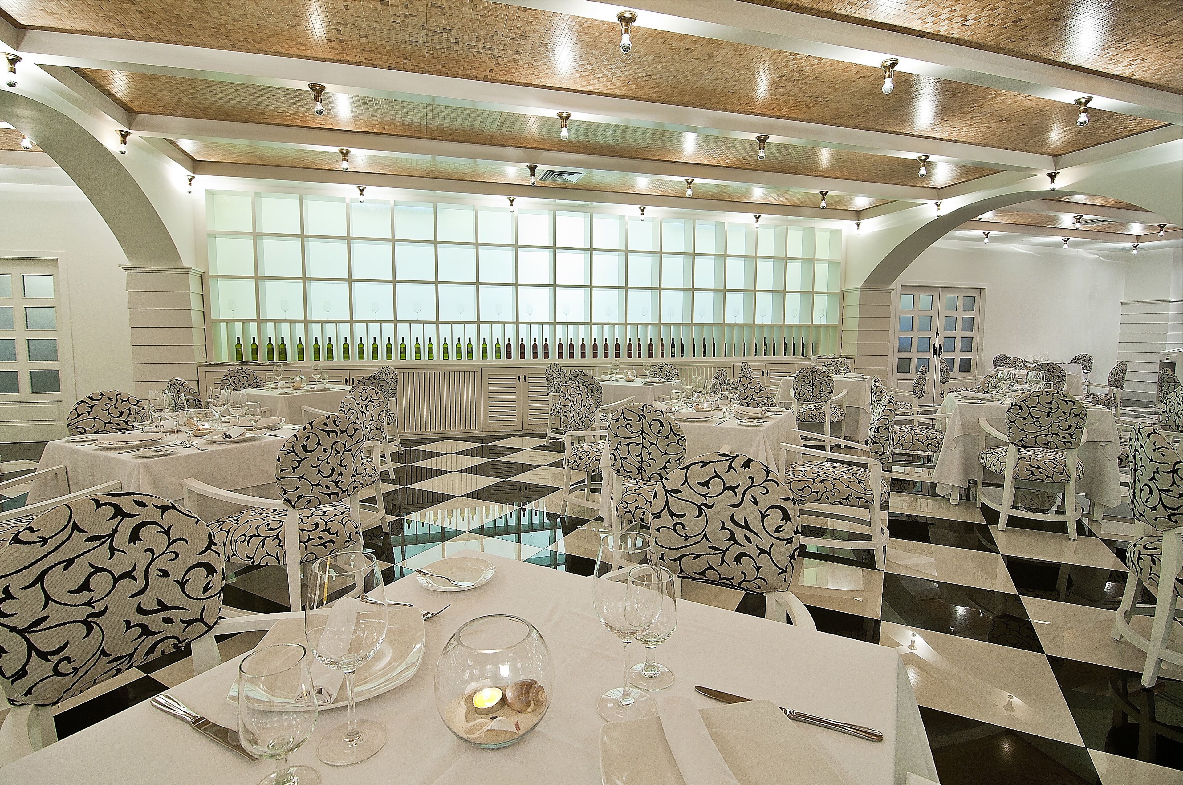 Un comedor con suelo a cuadros, mesas blancas y sillas con estampado blanco y negro.