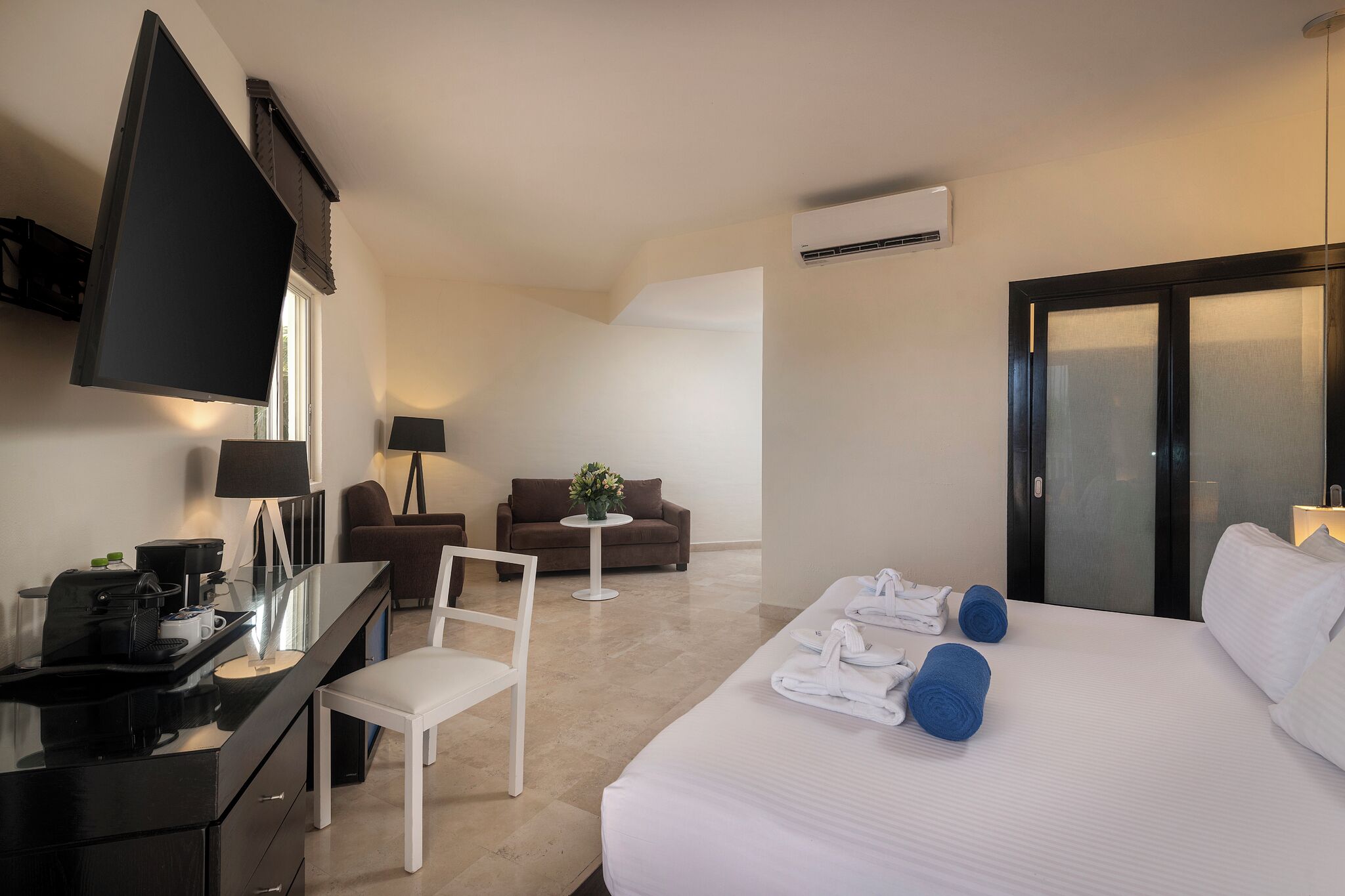Habitación de hotel con cama, escritorio, silla, sofá, una mesita y televisor.
