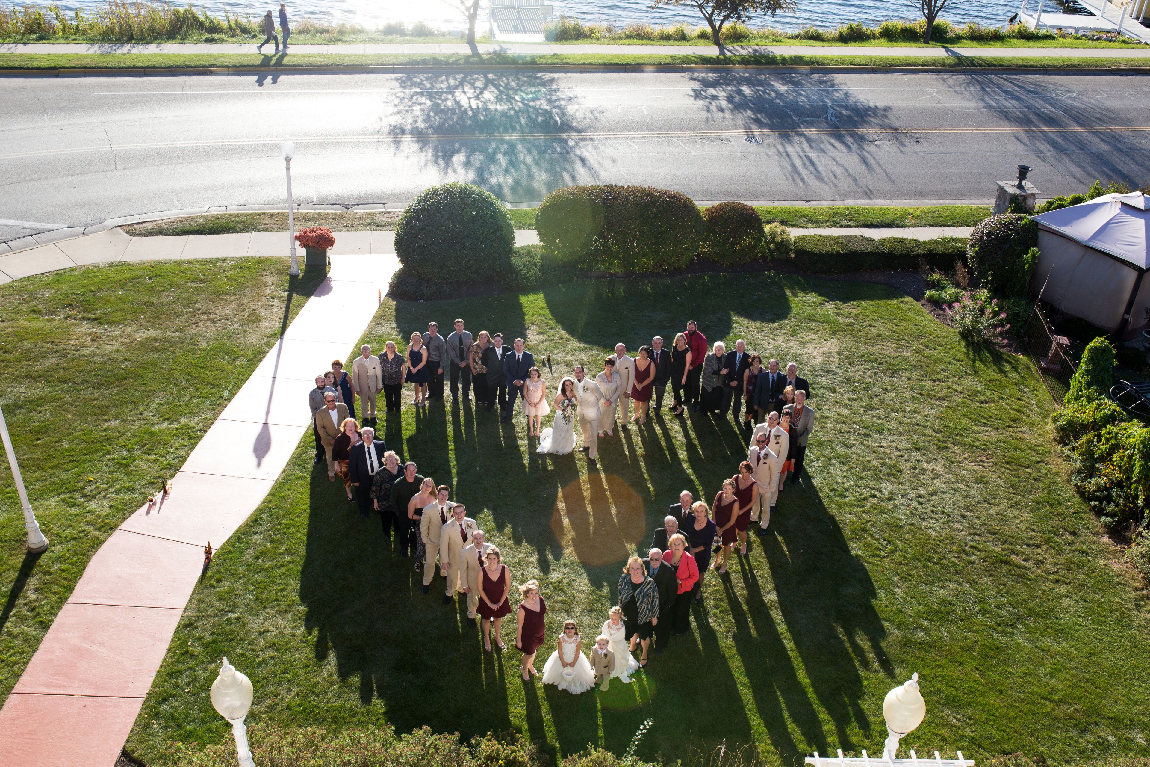 A group of people arranged in a heart shape on a grassy area with a sidewalk and street in the background.