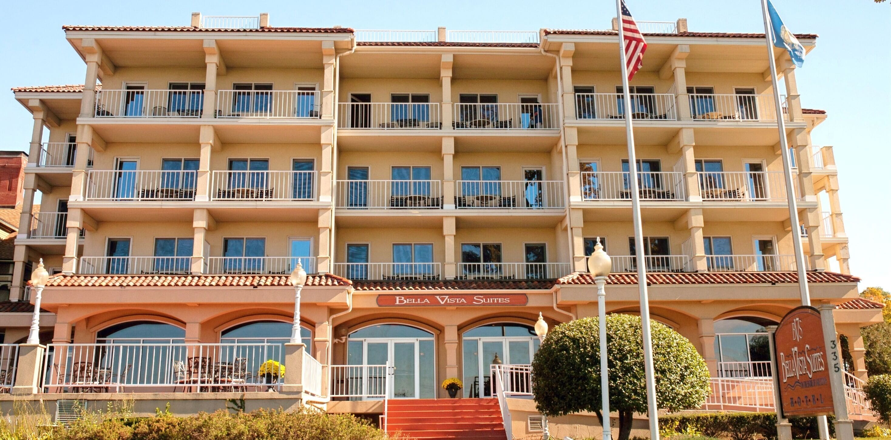 Un hotel de varios pisos con balcones, una bandera y un letrero que indica que es Bella Vista Suites.