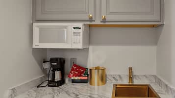 A compact kitchen with white cabinets, a built-in microwave, a coffee maker, a gold-colored sink, and a marble countertop.