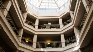 Un atrio de varios niveles con techo de cristal, balcones con barandillas y plantas en macetas.