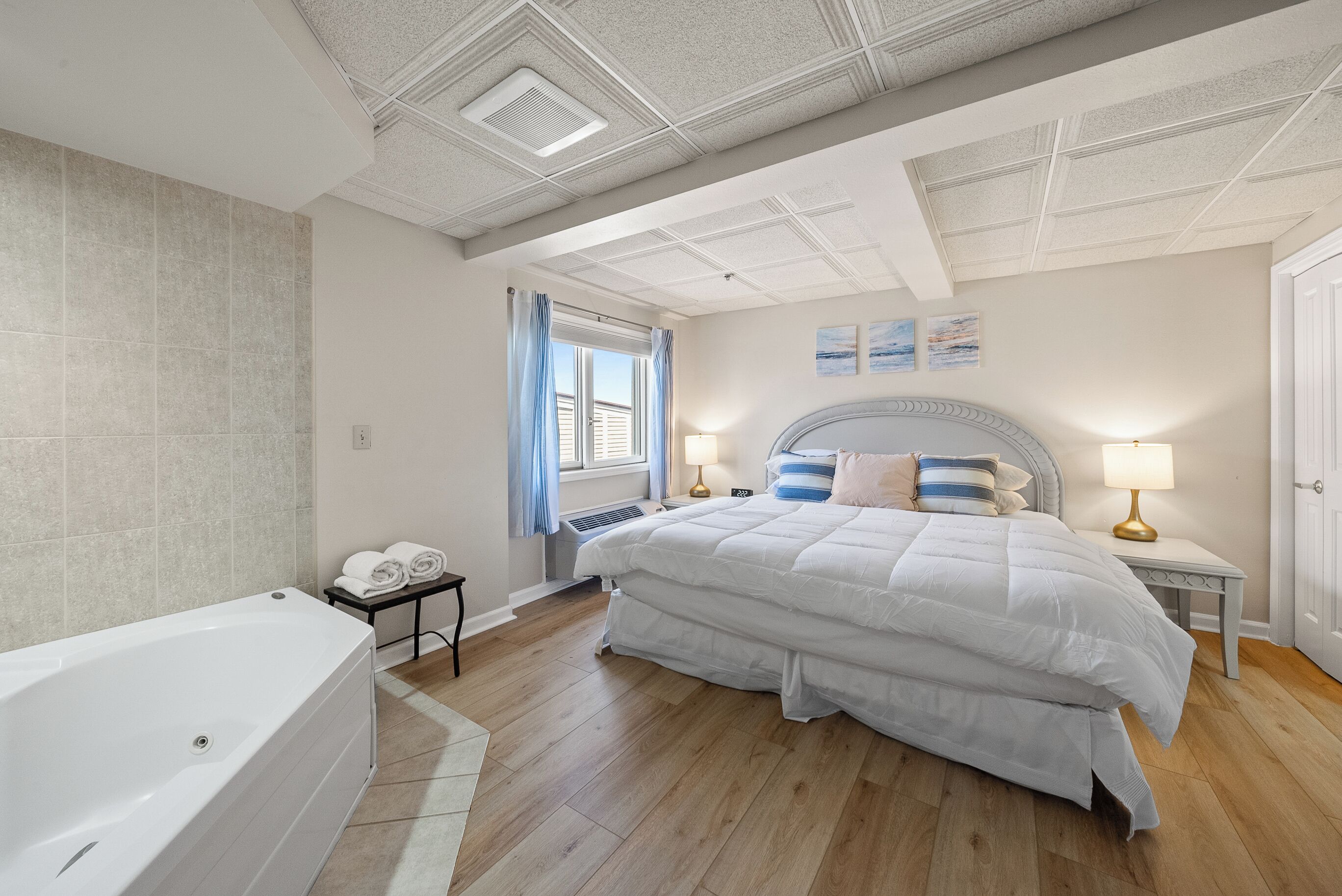 A bedroom with a large bed, a bathtub, and a window with curtains.
