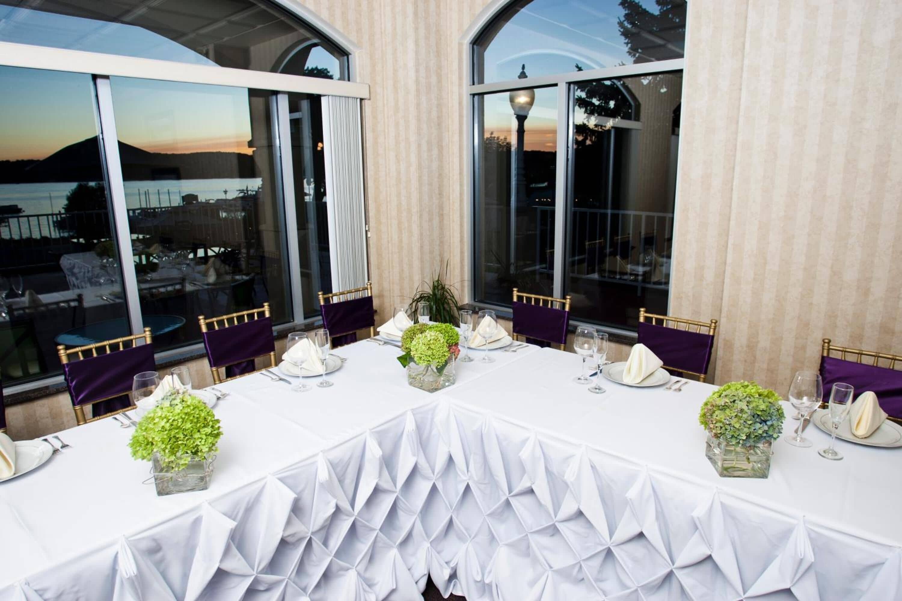 A table set for a meal with white tablecloths, green centerpieces, and purple chairs.