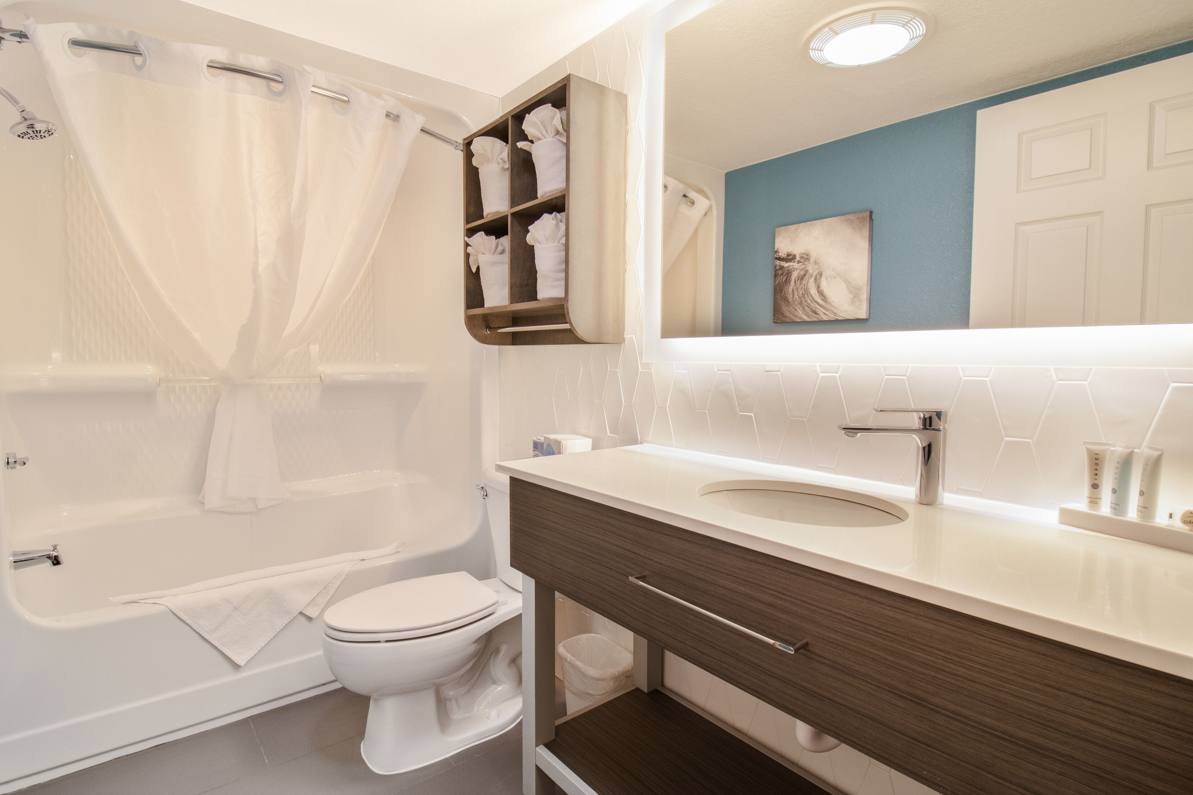 A modern bathroom with a bathtub, toilet, vanity, and a large mirror.