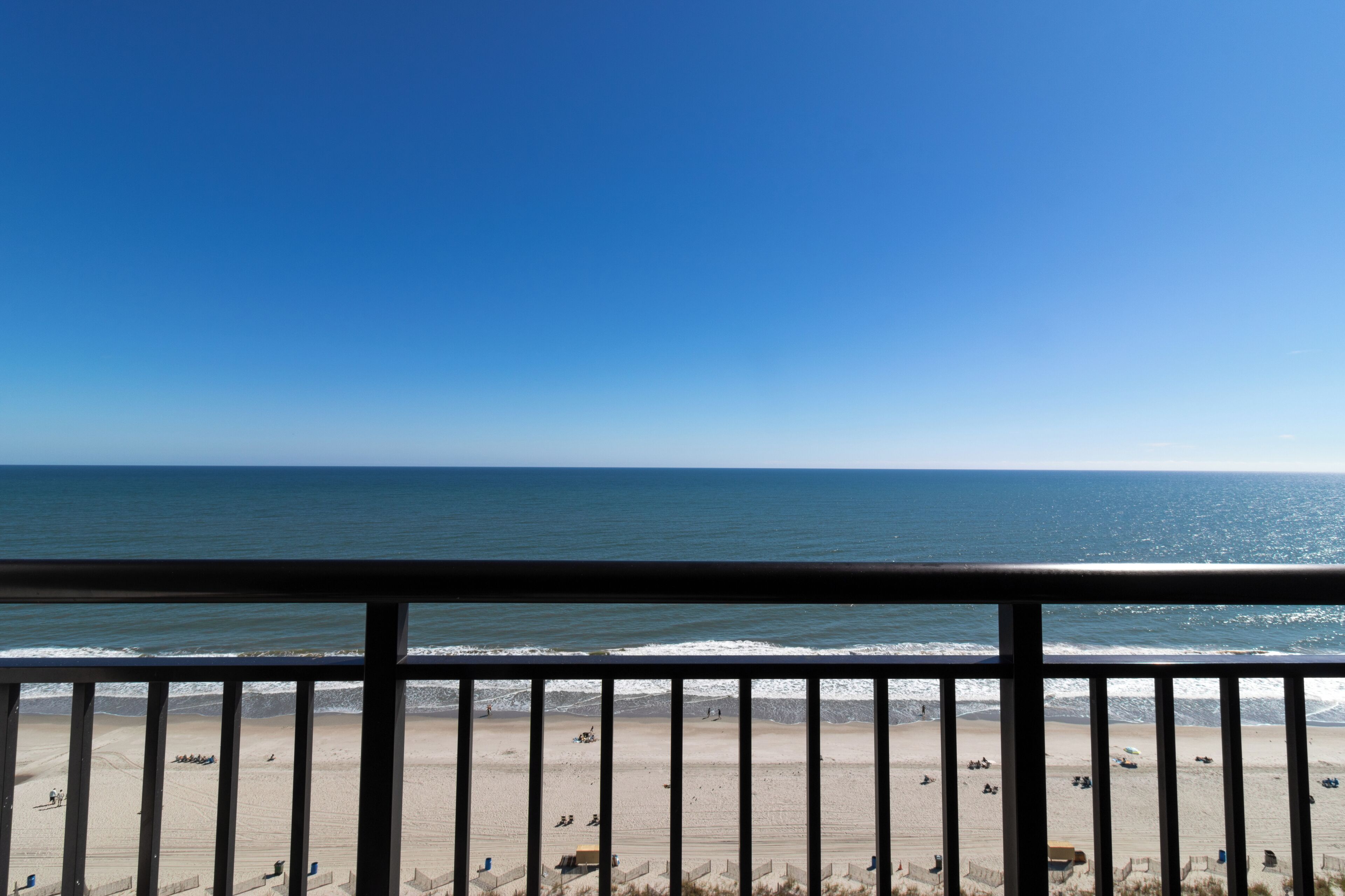 Una spiaggia con cielo sereno, una ringhiera in primo piano e vista sull'oceano.