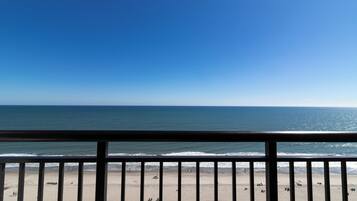 A beach with a clear sky, a railing in the foreground, and a view of the ocean.