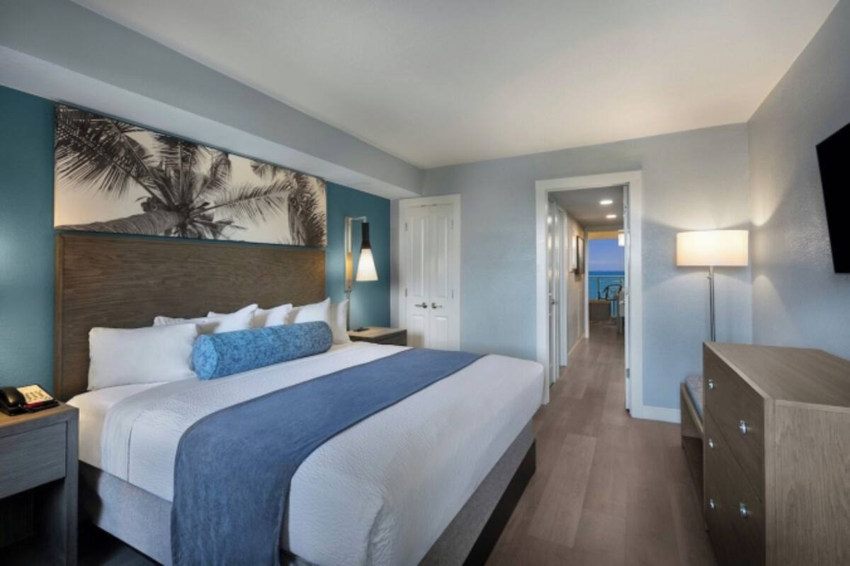 Camera d'albergo con un letto grande, un comodino con il telefono, una TV a parete e una porta che dà su un'altra stanza.
