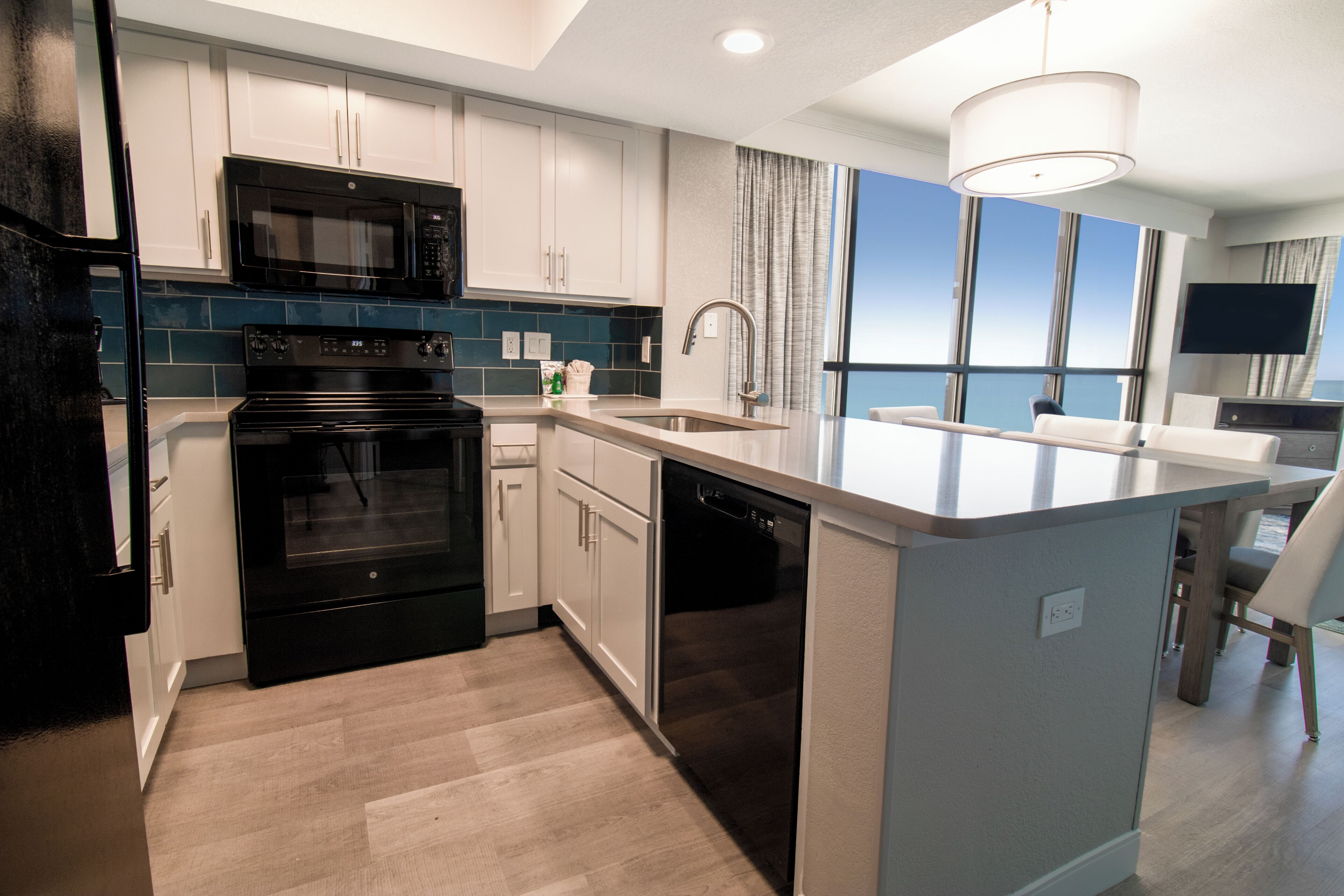 A modern kitchen with a built-in microwave, oven, and dishwasher, a large island with a sink, and a view of the ocean through large windows.