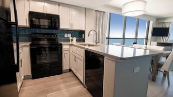 Una cocina moderna con microondas, horno y lavavajillas integrados, una isla grande con fregadero y vistas al océano a través de amplios ventanales.