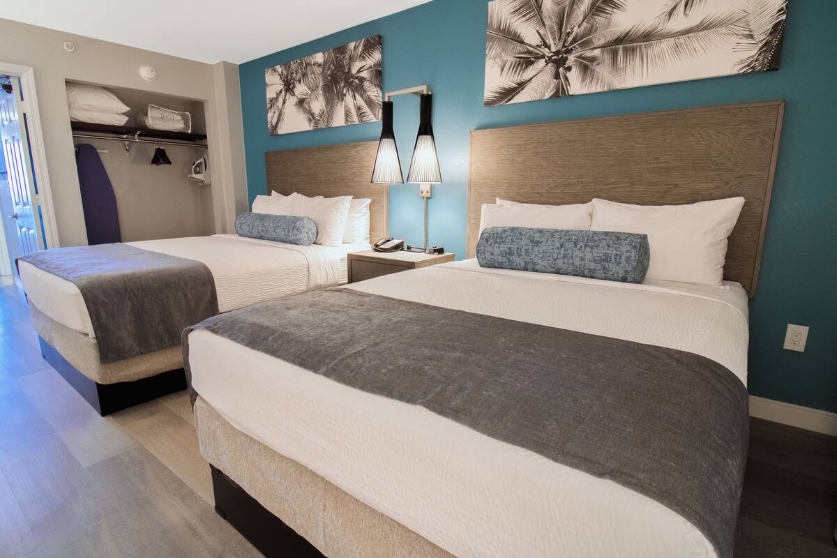 Una camera d'albergo con due letti, un comodino con una lampada, un armadio e una porta che dà sull'esterno.