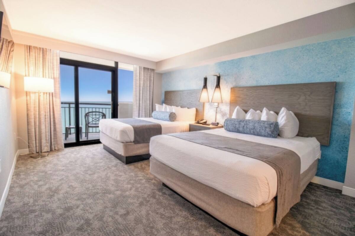 Una camera d'albergo con due letti, un balcone e vista sull'oceano.