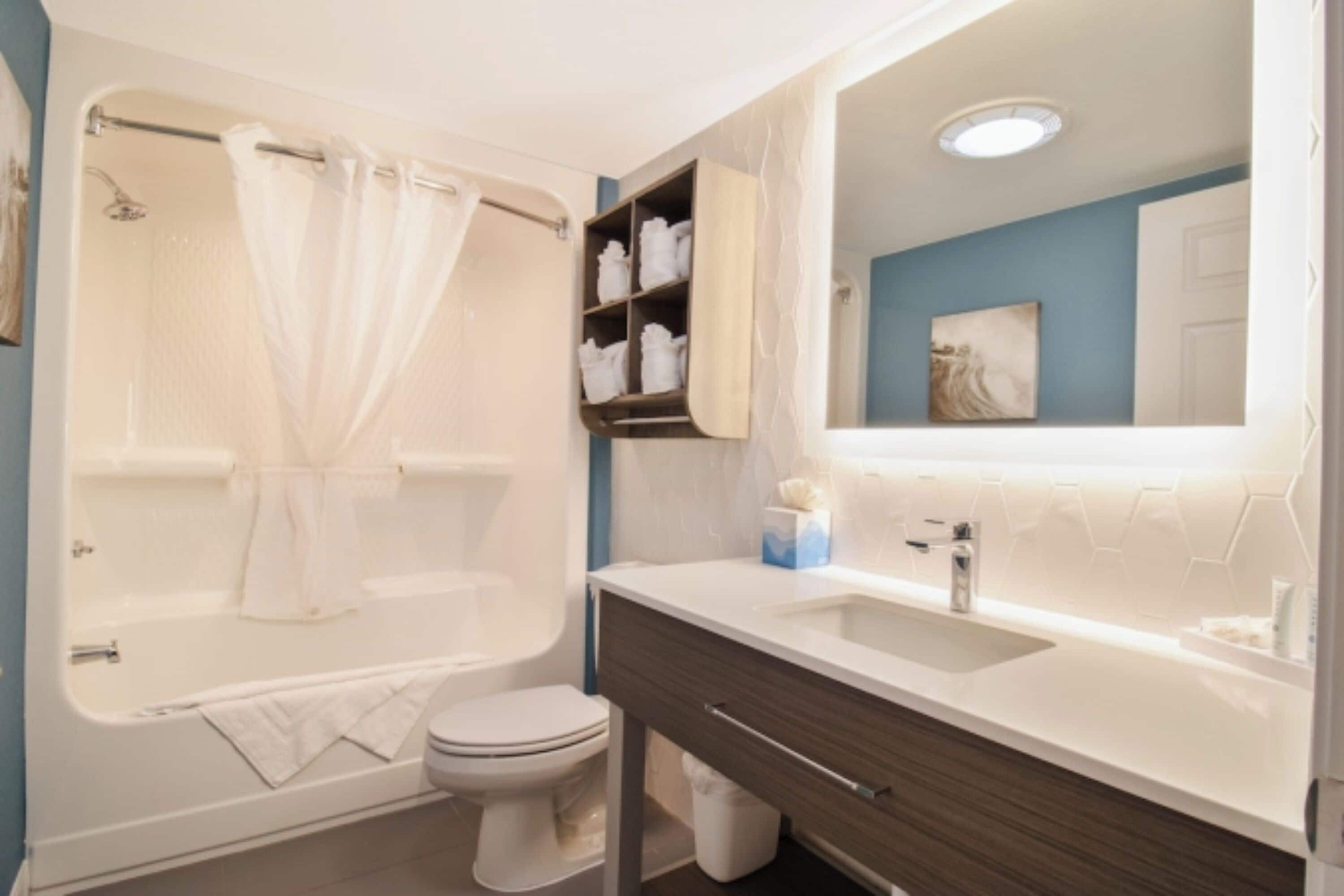 A modern bathroom with a bathtub, toilet, vanity, and a large mirror.