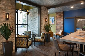 A modern interior with a stone wall, wooden flooring, and a mix of seating arrangements including a long table and chairs.