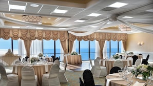 A banquet hall with round tables, white chairs, and a view of the ocean.