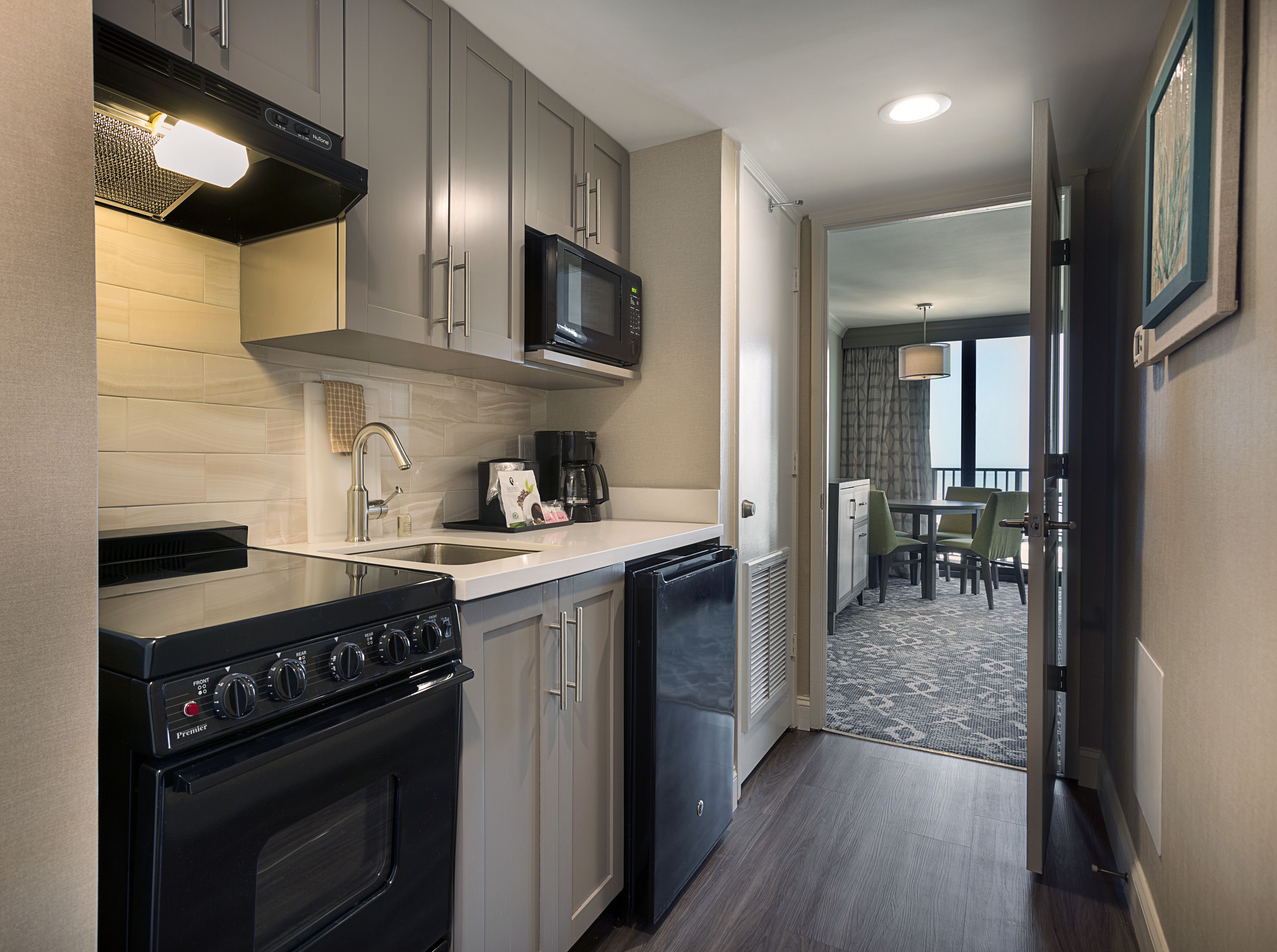 A compact kitchen with a microwave, stove, and sink. There's a dining area with a table and chairs visible through an open door.