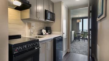 A compact kitchen with a microwave, stove, and sink. There's a dining area with a table and chairs visible through an open door.