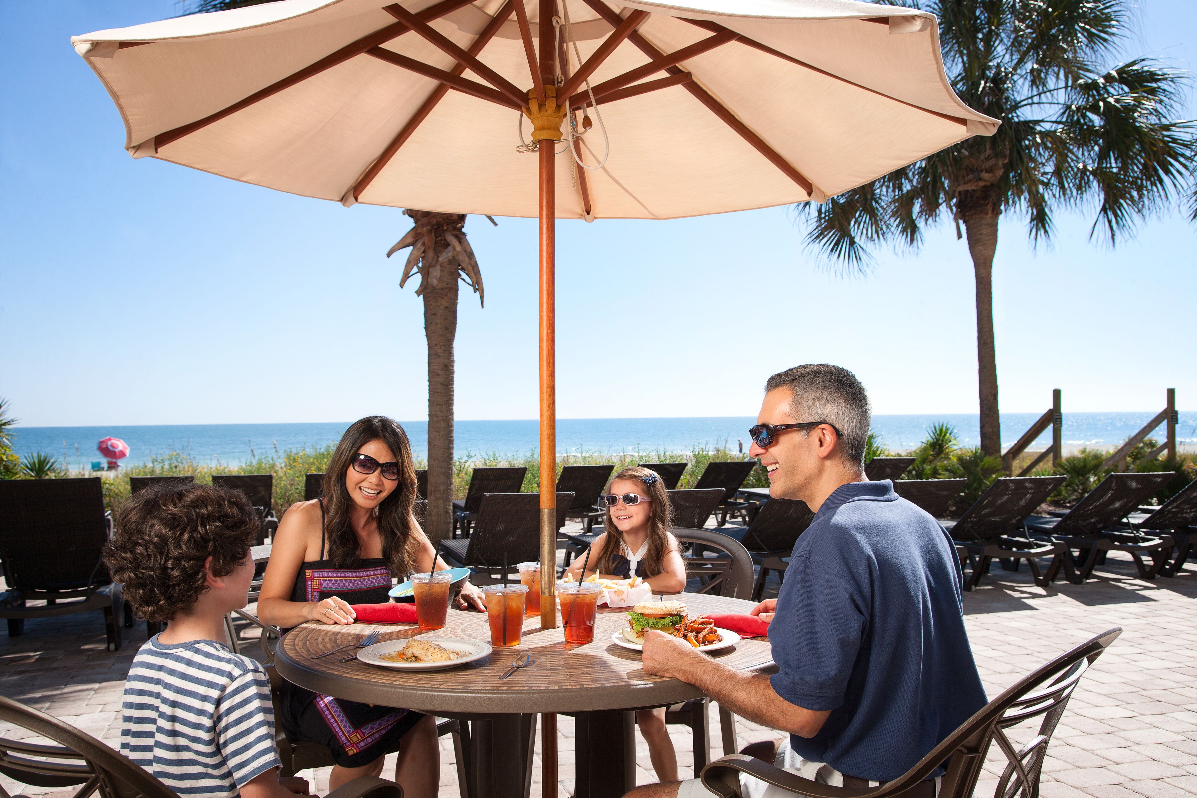A family dining at an outdoor table with a view of the ocean.