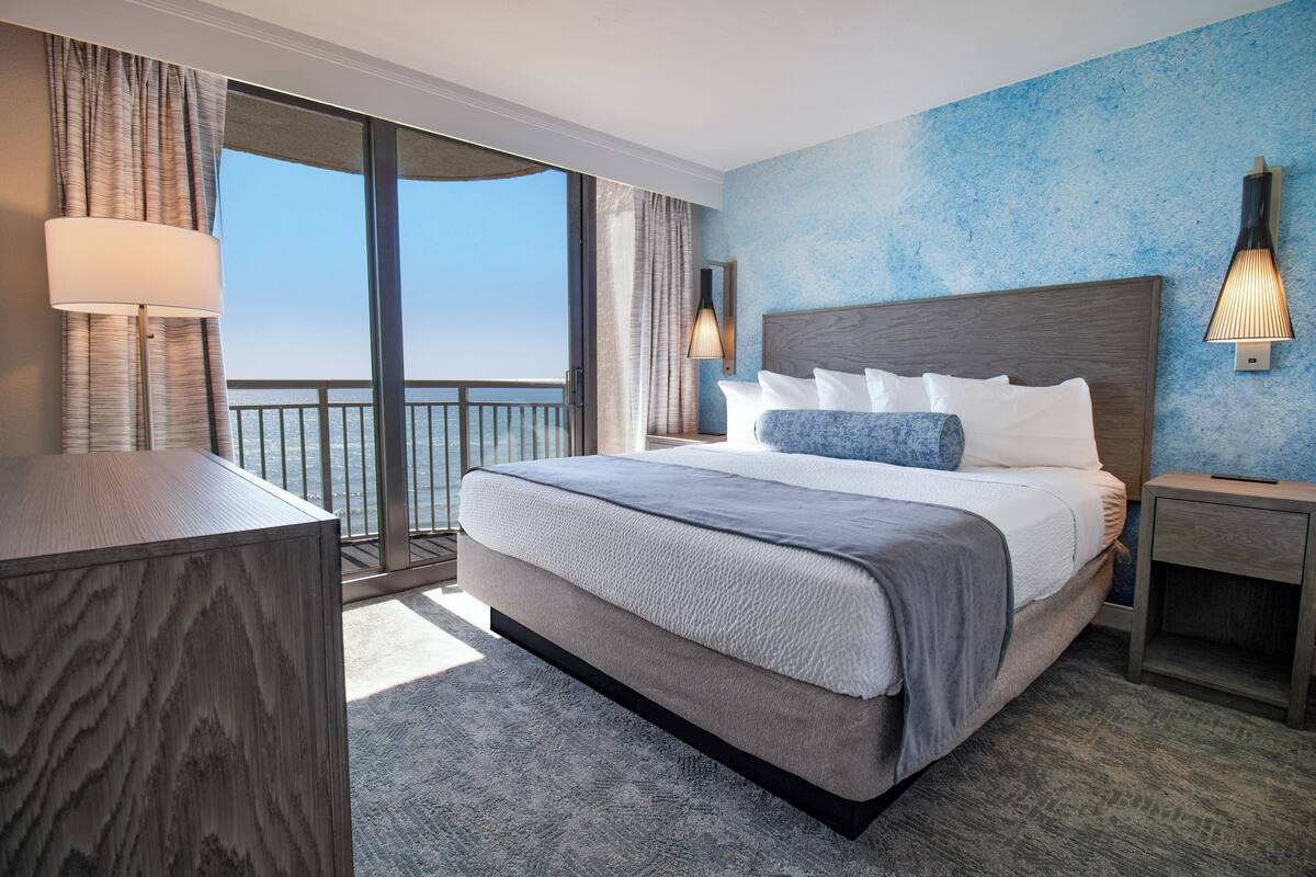 Camera d'albergo con un ampio letto, un comodino, una lampada e vista sull'oceano.