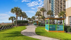 Un camino que conduce a una zona de piscina con tumbonas, un área de juegos infantiles y altos edificios residenciales.