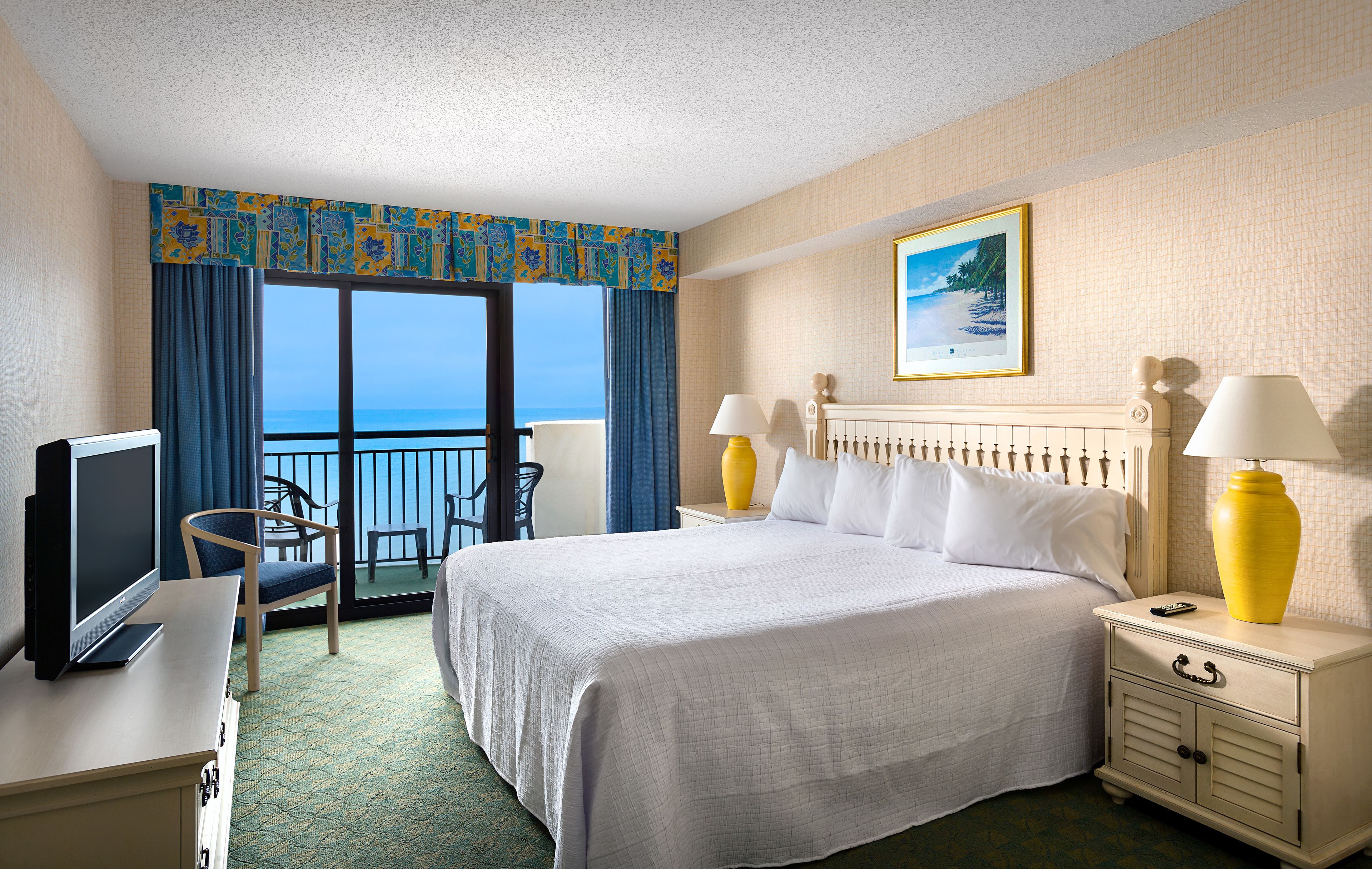 A hotel room with a large bed, two bedside lamps, a TV, a desk, and a chair.