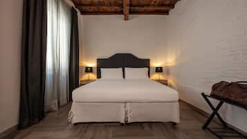 Een slaapkamer met een houten plafond, een groot bed met witte beddengoed, twee bedlampjes en een bruine lederen tas op een standaard.