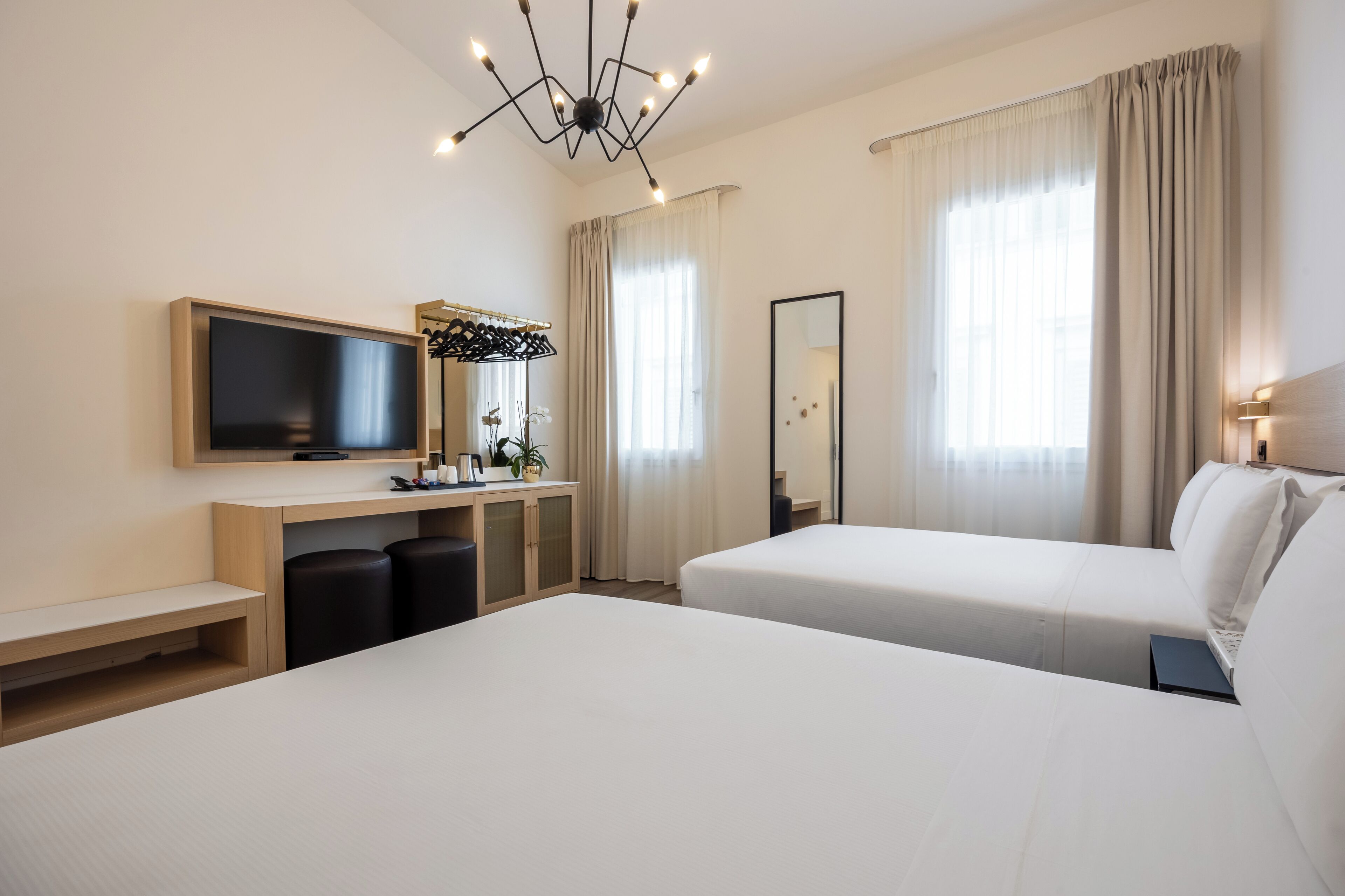 Habitación de hotel con dos camas, televisión, escritorio con espejo y candelabro.