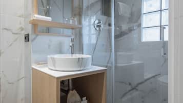 Un baño moderno con lavamanos de mármol, tocador de madera y ducha con mampara de vidrio.