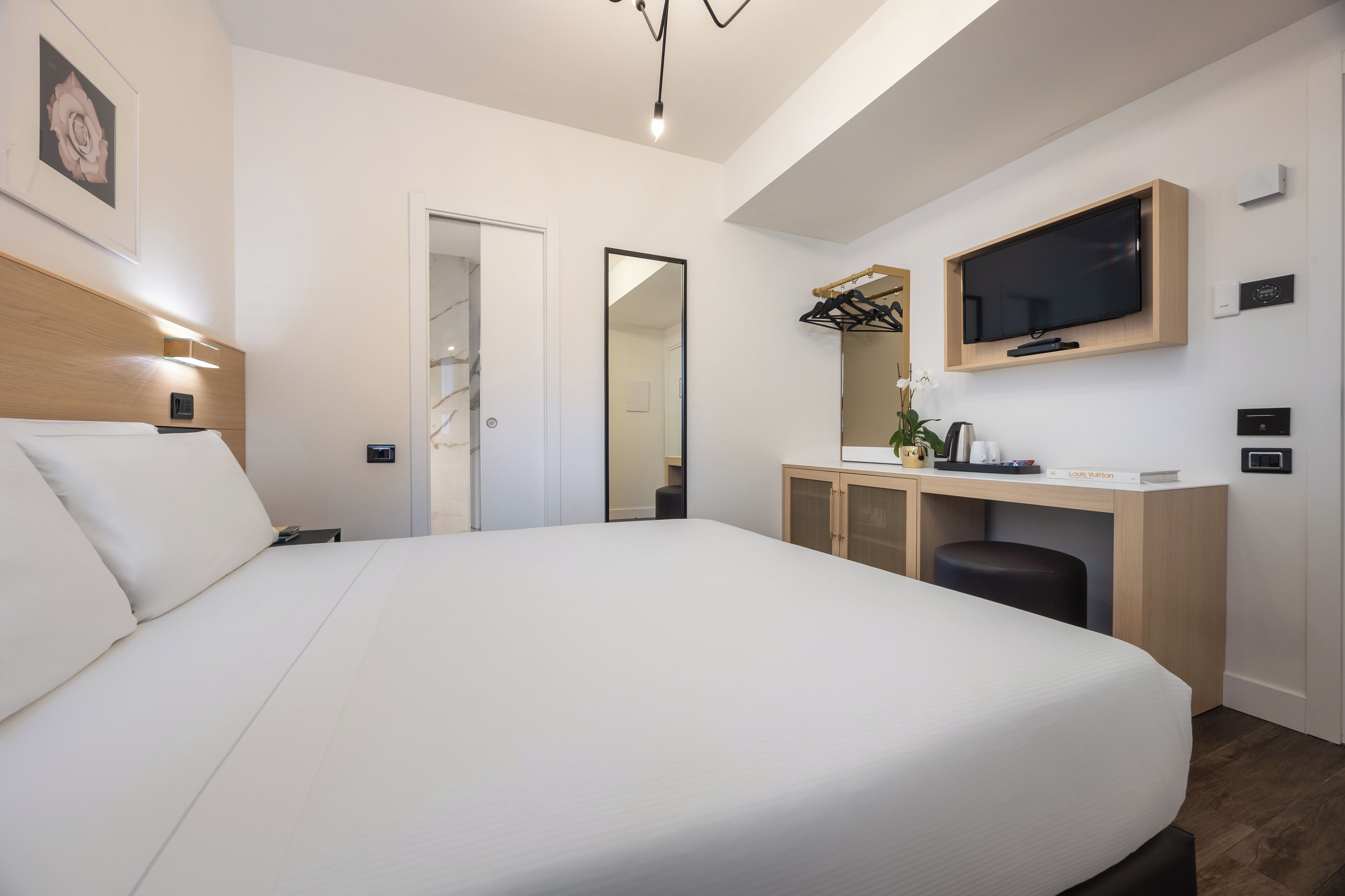 Una habitación de hotel moderna con una cama grande, un escritorio con televisor y un vestidor.