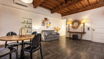 Zona pranzo con tavolo e sedie in legno, divano grigio con cuscini decorativi ed una mensola a parete con piante in vaso.