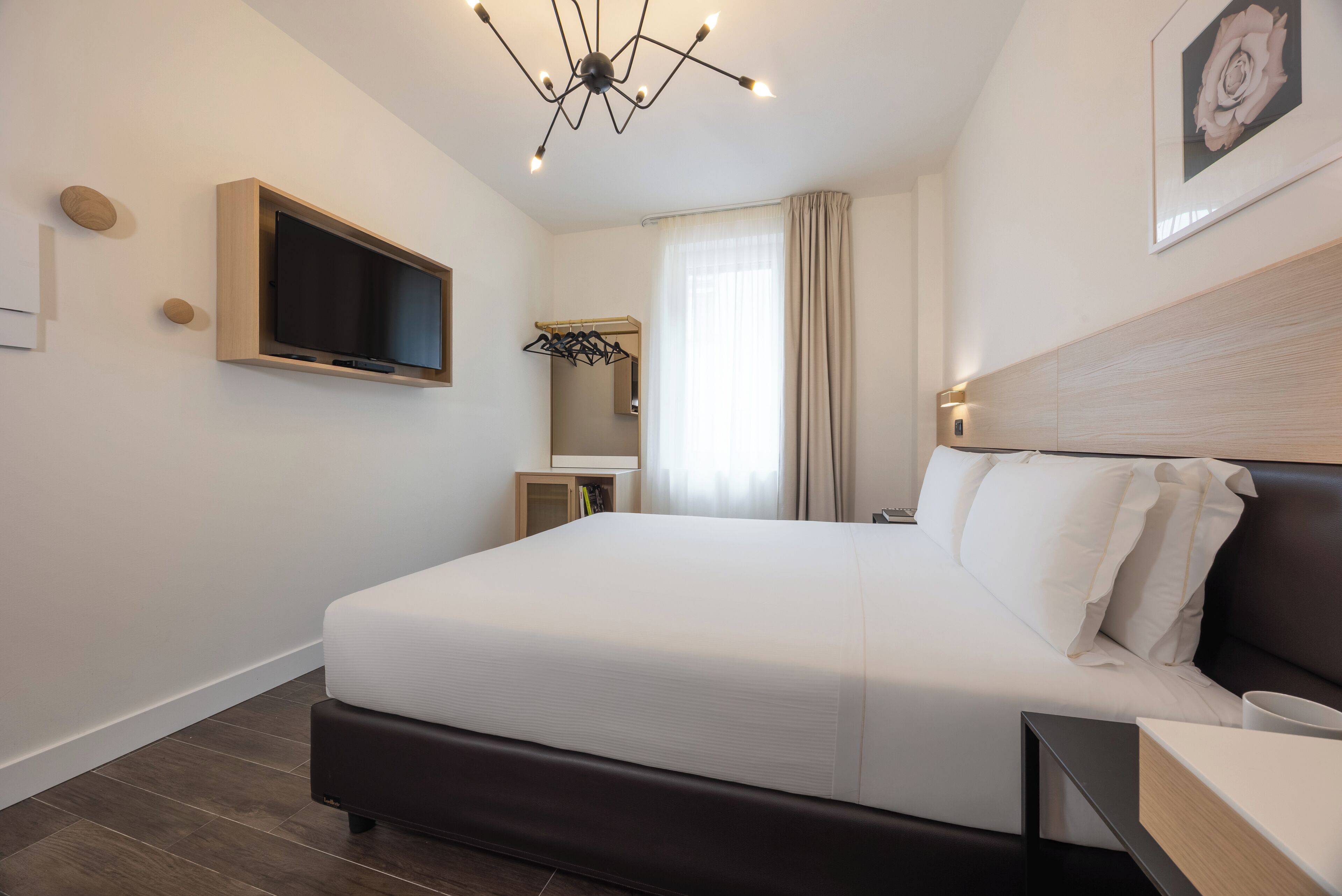 A modern hotel room with a large bed, a television mounted on the wall, a bedside table, and a wardrobe with a mirror.